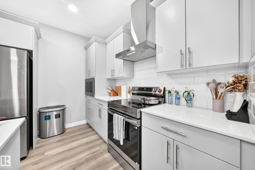 White shaker-style cabinetry with chrome hardware, stainless steel appliances, white subway tile backsplash, light wood-finish flooring, and solid surface countertops - 2415 194 Street Nw, Edmonton, AB 