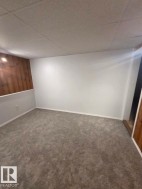 Textured gray carpeting, white walls, wood panel accent wall, and a drop ceiling - 
