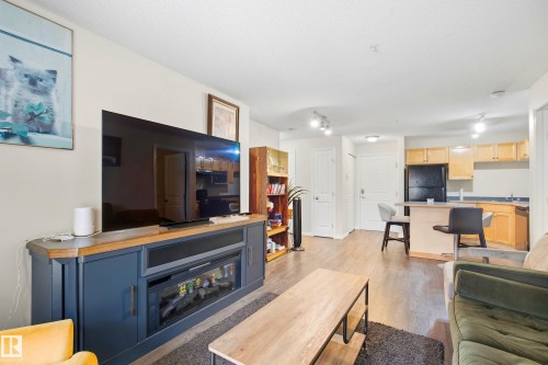 Wood-finish flooring throughout, light-toned walls, recessed lighting, and a built-in media console with an electric fireplace - #203 245 Edwards Dr Sw, Edmonton, AB 