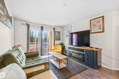 Sliding glass doors opening to an outdoor patio, wood-finish flooring, and a built-in media console - #203 245 Edwards Dr Sw, Edmonton, AB 