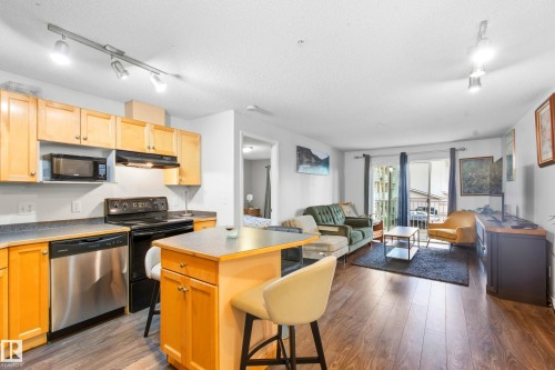 Wood-finish flooring throughout, track lighting, light wood cabinetry, stainless steel dishwasher, and a sliding glass door - #203 245 Edwards Dr Sw, Edmonton, AB 