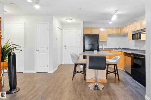Kitchen featuring light wood-finish cabinetry, dark countertops, and black appliances - #203 245 Edwards Dr Sw, Edmonton, AB 