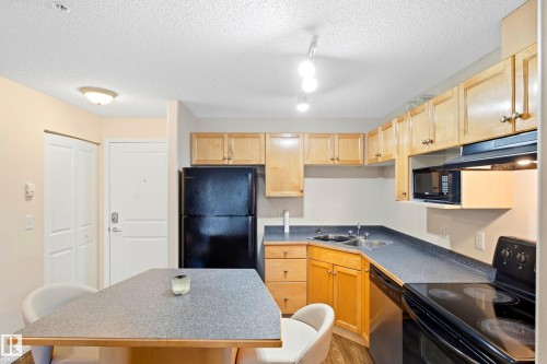 Kitchen featuring wood-finish cabinetry, black appliances, track lighting, and a built-in microwave - #203 245 Edwards Dr Sw, Edmonton, AB 