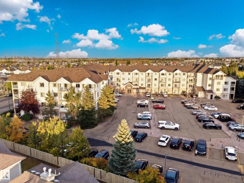 Multi-story residential building featuring balconies, a parking lot, and surrounding mature landscaping - #203 245 Edwards Dr Sw, Edmonton, AB 