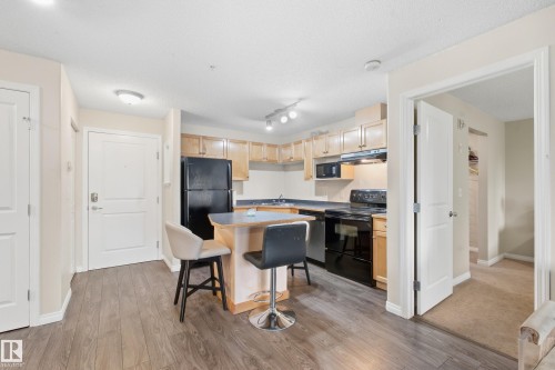 Kitchen with wood-finish flooring, black appliances, light wood cabinetry, and a peninsula with countertop seating - #203 245 Edwards Dr Sw, Edmonton, AB 