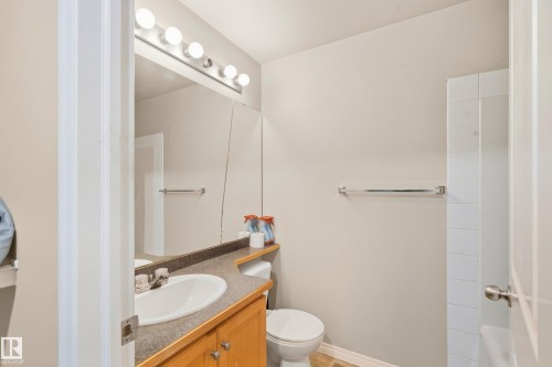 Vanity with wood-finish cabinetry, integrated sink, and dark countertop - #203 245 Edwards Dr Sw, Edmonton, AB 