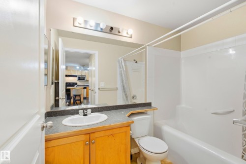Bathroom featuring a single vanity with wood-finish cabinetry, a white oval sink, and a dark-toned countertop - #203 245 Edwards Dr Sw, Edmonton, AB 
