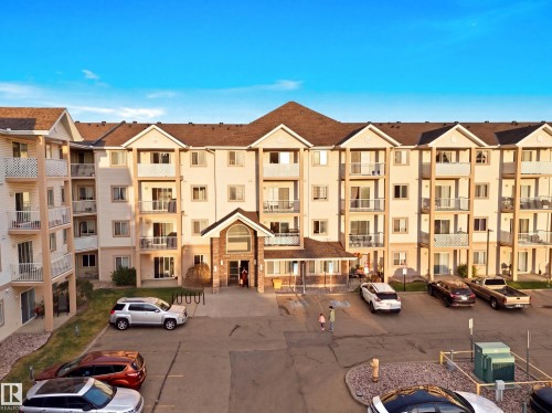 Multi-story building featuring individual balconies, a prominent main entrance with a covered portico, and a pitched roofline - #203 245 Edwards Dr Sw, Edmonton, AB 