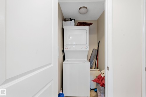 Laundry area with a stacked washer and dryer unit, and a ceiling-mounted light fixture - #203 245 Edwards Dr Sw, Edmonton, AB 
