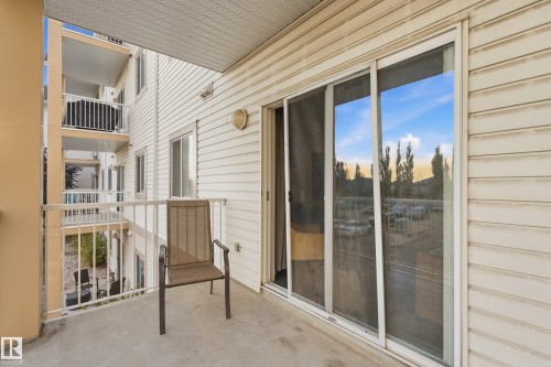 Balcony with concrete flooring and white metal railings, featuring white siding exterior, and a sliding glass door with a screen - #203 245 Edwards Dr Sw, Edmonton, AB 