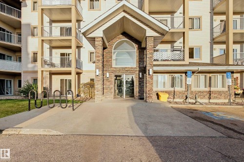 Building exterior featuring a stone-clad entrance, multiple balconies, a covered entryway, and accessible ramps - #203 245 Edwards Dr Sw, Edmonton, AB 