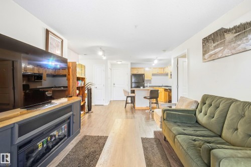 Open concept living area featuring wood-finish flooring, a built-in fireplace unit, track lighting, and a kitchen with wood cabinetry - #203 245 Edwards Dr Sw, Edmonton, AB 