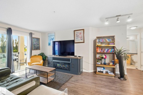 Wood-finish flooring throughout, sliding glass door leading to a balcony, built-in media console, and recessed lighting - #203 245 Edwards Dr Sw, Edmonton, AB 