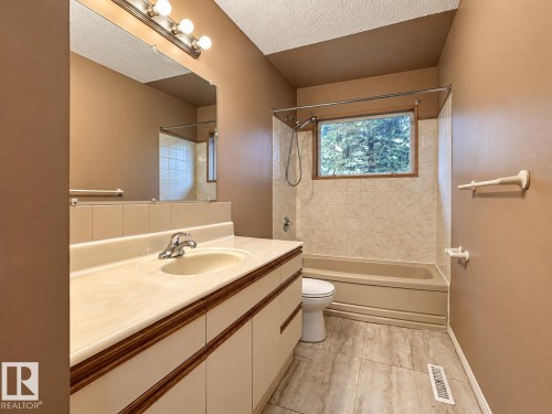 Bathroom featuring a vanity with an integrated sink, a large wall mirror, and a shower-bathtub combination with a tiled surround - 12204 40 Avenue Nw, Edmonton, AB 