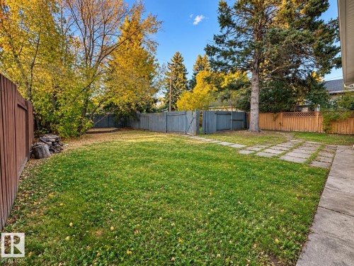 Expansive grassy area with mature trees, surrounded by fencing, and featuring square paver pathways - 12204 40 Avenue Nw, Edmonton, AB 