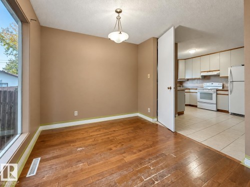 Hardwood flooring, large window, neutral wall tones, overhead lighting fixture, and access to kitchen with white appliances - 12204 40 Avenue Nw, Edmonton, AB 