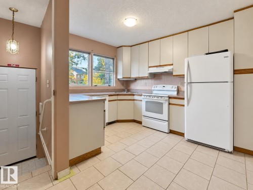 Kitchen featuring tile flooring, white appliances, corner sink, and white cabinetry - 12204 40 Avenue Nw, Edmonton, AB 