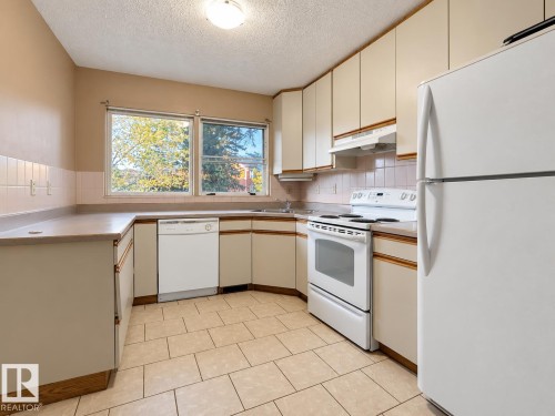 Kitchen featuring tile flooring, white appliances, L-shaped countertops, and upper and lower cabinetry - 12204 40 Avenue Nw, Edmonton, AB 