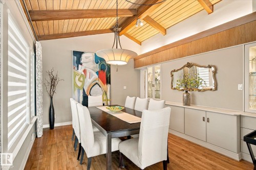 Vaulted wood-paneled ceiling with exposed beams, wood-finish flooring, built-in cabinetry with glass display, and a decorative pendant light fixture - 13862 Ravine Drive Nw, Edmonton, AB 
