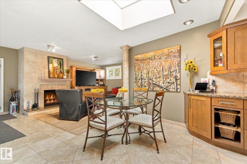 Travertine tile flooring, built-in corner cabinetry with glass-front uppers, granite-look countertops, a skylight, and a tiled fireplace with a mantel - 13862 Ravine Drive Nw, Edmonton, AB 