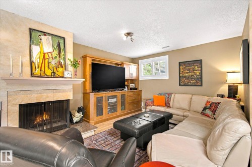 Stone-surround fireplace with hearth, wood-finish entertainment center, and a single window with white louvered shutters - 13862 Ravine Drive Nw, Edmonton, AB 