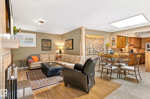 Open-concept living space featuring a fireplace with a stone surround, recessed lighting, and a kitchen with wood cabinetry and stainless steel appliances - 13862 Ravine Drive Nw, Edmonton, AB 