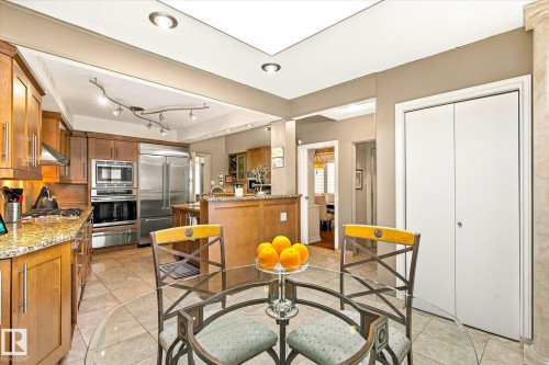 Kitchen with wood cabinetry, stainless steel appliances, granite countertops, and tiled flooring - 13862 Ravine Drive Nw, Edmonton, AB 