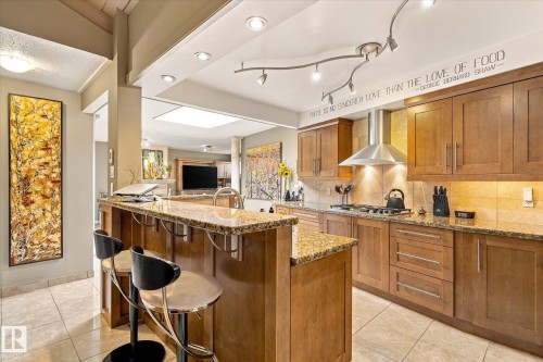 Kitchen featuring wood-finish cabinetry, granite countertops, tile flooring, and a stainless steel range hood - 13862 Ravine Drive Nw, Edmonton, AB 