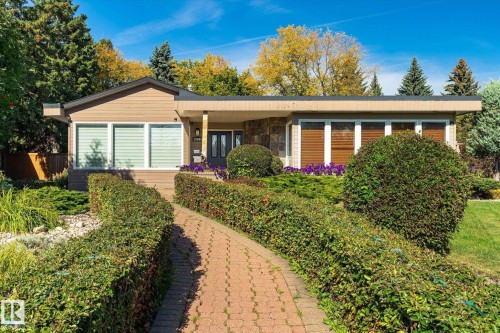 Mid-century modern exterior featuring a flat roofline, stone facade accents, and a paved walkway - 13862 Ravine Drive Nw, Edmonton, AB 
