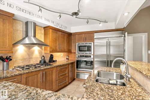 Wood-finish cabinetry, stainless steel appliances, tile backsplash, granite countertops, and built-in sink with gooseneck faucet - 13862 Ravine Drive Nw, Edmonton, AB 