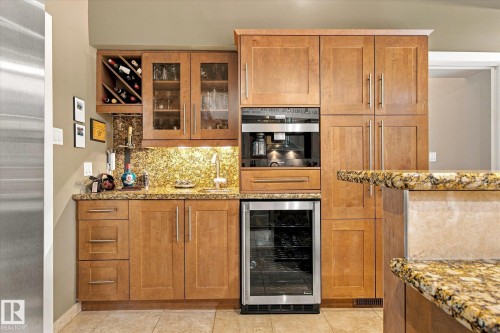 Built-in bar area featuring wood cabinetry, integrated wine storage, under-cabinet lighting, and a built-in beverage cooler - 13862 Ravine Drive Nw, Edmonton, AB 