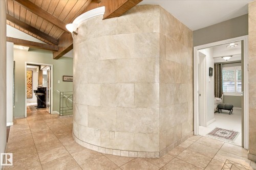 Vaulted wood-paneled ceiling with exposed beams, tiled flooring, curved stone-tiled wall, and metal railing with decorative elements - 13862 Ravine Drive Nw, Edmonton, AB 