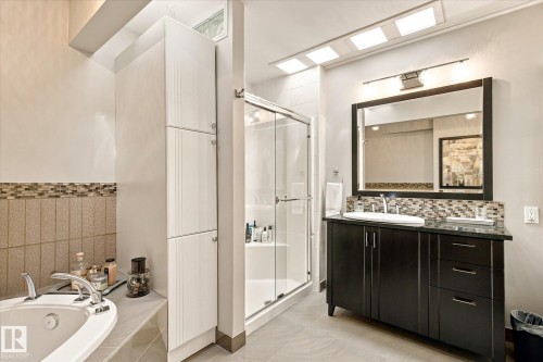 Bathroom featuring an integral jetted tub, glass-enclosed shower, dark wood-finish vanity with an undermount sink, and extensive built-in storage cabinetry - 13862 Ravine Drive Nw, Edmonton, AB 
