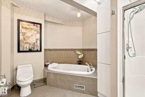 Built-in soaking tub with deck-mounted fixtures, glass-enclosed shower, white toilet, and tile flooring - 13862 Ravine Drive Nw, Edmonton, AB 