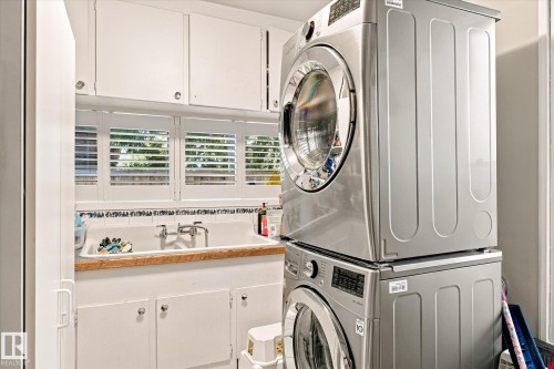 Laundry area featuring white cabinetry, a sink with a wood-finish countertop, white window shutters, and a stacked washer and dryer - 13862 Ravine Drive Nw, Edmonton, AB 