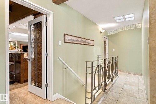 Hallway featuring patterned metal railing, tiled flooring, glass block wall accent, and a decorative glass door - 13862 Ravine Drive Nw, Edmonton, AB 