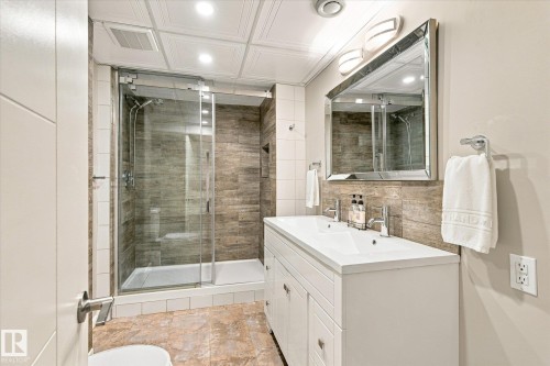 Walk-in shower with sliding glass door, dual sink vanity with white cabinetry, wood-look tile shower surround, and tile flooring - 13862 Ravine Drive Nw, Edmonton, AB 