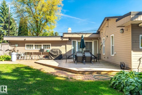 Expansive backyard featuring a manicured lawn, brick paver path, raised patio deck, and sliding glass doors - 13862 Ravine Drive Nw, Edmonton, AB 