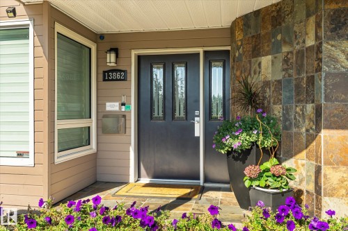 Entryway featuring a dark paneled door with decorative glass inserts, natural stone tile accent wall, horizontal siding, and a modern exterior light fixture - 13862 Ravine Drive Nw, Edmonton, AB 
