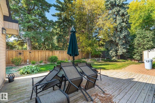 Wood-finish deck with a stone paver patio, surrounded by a wood fence, mature trees, and landscaping - 13862 Ravine Drive Nw, Edmonton, AB 