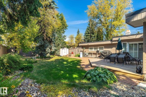 Expansive lawn area with mature trees, brick paver patio, wood deck, and an exterior storage shed - 13862 Ravine Drive Nw, Edmonton, AB 