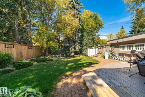 Expansive backyard featuring a manicured lawn, brick paver pathway, and a wooden deck - 13862 Ravine Drive Nw, Edmonton, AB 