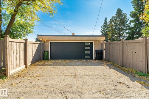 Detached garage with a dark-paneled door, frosted rectangular windows, and light-colored siding - 13862 Ravine Drive Nw, Edmonton, AB 