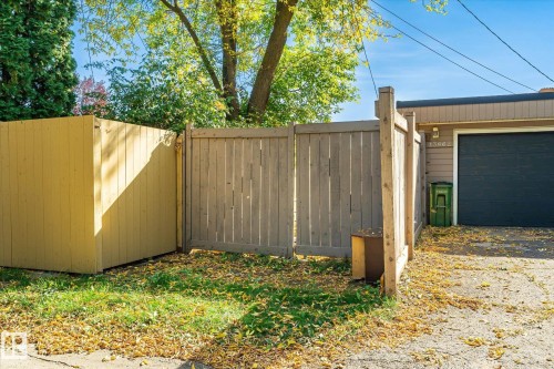 Wood privacy fence with double gates leading to a paved surface and a garage with a black roll-up door - 13862 Ravine Drive Nw, Edmonton, AB 