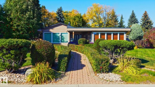 Single-story residence featuring a brick paver walkway, mature landscaping, and a manicured lawn - 13862 Ravine Drive Nw, Edmonton, AB 