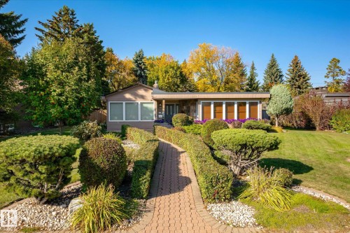 Exterior featuring an extensive brick paver walkway, mature landscaping with manicured shrubs, and a well-maintained lawn - 13862 Ravine Drive Nw, Edmonton, AB 