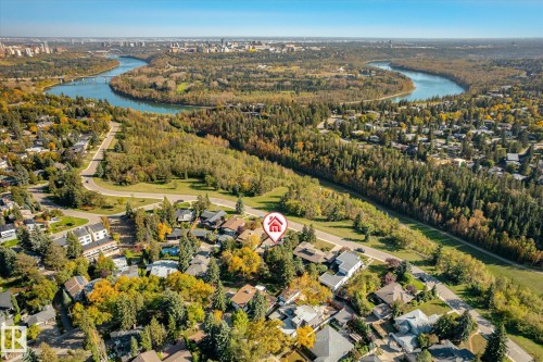 Aerial perspective of a residential area featuring mature trees, a winding river, and distant urban skyline - 13862 Ravine Drive Nw, Edmonton, AB 