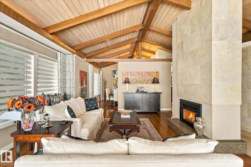 Vaulted wood-paneled ceiling with exposed beams, wood-finish flooring, stone-clad fireplace with hearth, and window treatments - 13862 Ravine Drive Nw, Edmonton, AB 
