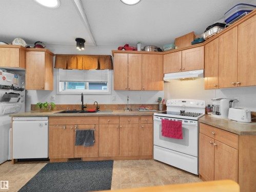 Light wood-finish cabinetry, solid surface countertops, a stainless steel sink with a matte black faucet, and white appliances - 52 Evergreen Park Northwest, Edmonton, AB 