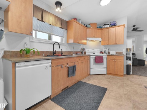 U-shaped kitchen with wood-finish cabinetry, light-toned countertops, and a tile backsplash - 52 Evergreen Park Northwest, Edmonton, AB 